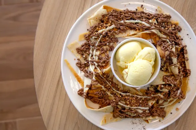 A view from above of crepes with chocolate sauce and two scoops of ice cream in a small bowl