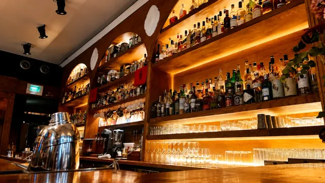 Lit wooden shelves loaded with bottles, rows of glasses and a shaker on the counter