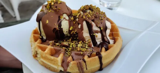 A Belgian waffle with scoops of ice cream, chocolate sauce and crushed pistachio on top