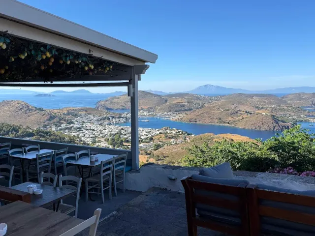 Tables under a canopy decorated with lemons, facing a bay and a white town on a hill