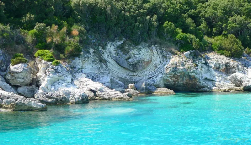 Glowing turquoise water against curved white limestone rocks with green scrub above