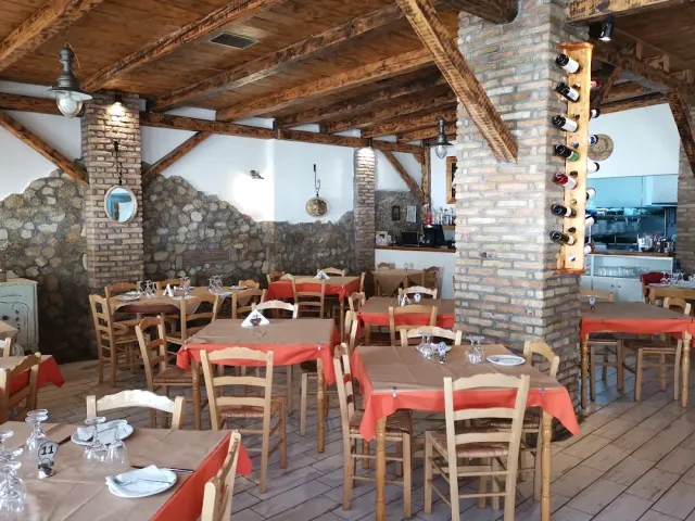 An interior with wooden beams, brick columns and a stone wall, tables with brown and red cloths
