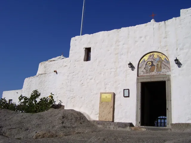 The white front of a monastery with an arched gate and a mosaic above it