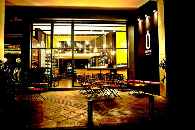 A glass front lit at night, with colourful folding chairs on a paved forecourt