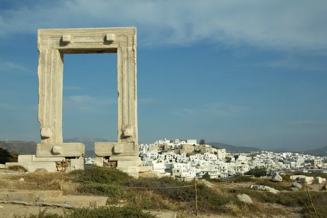 A lone ancient marble gate standing on a hill, with a white town and the sea behind