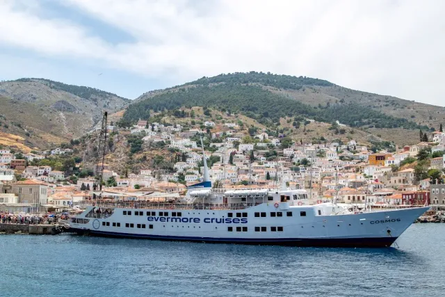 A white passenger ship moored before an island town of tiled roof houses on a slope