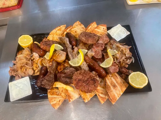 A large platter of grilled meats, sausages and pitas with lemon wedges and sauce