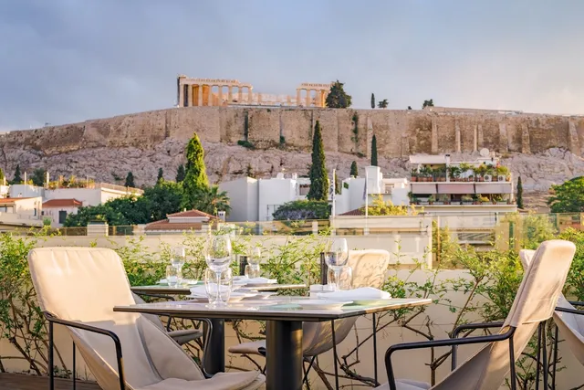 Set tables on a rooftop with greenery, facing the Acropolis hill and the Parthenon