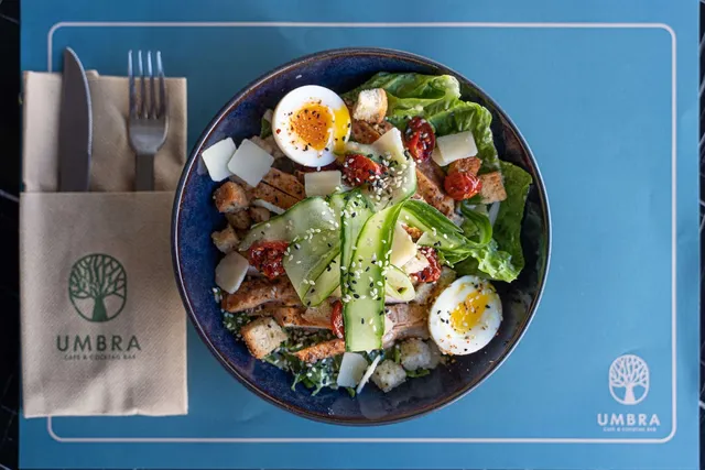 A salad bowl with chicken, eggs, croutons and cucumber on a blue placemat