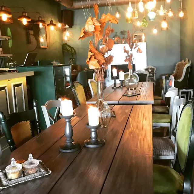 A long wooden table with candles, assorted upholstered chairs and hanging bulbs in the room