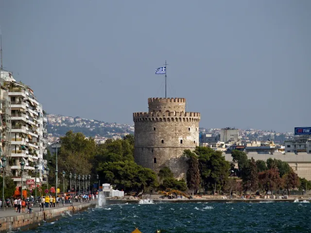 A round pale stone tower on the seafront, with trees and a promenade around it