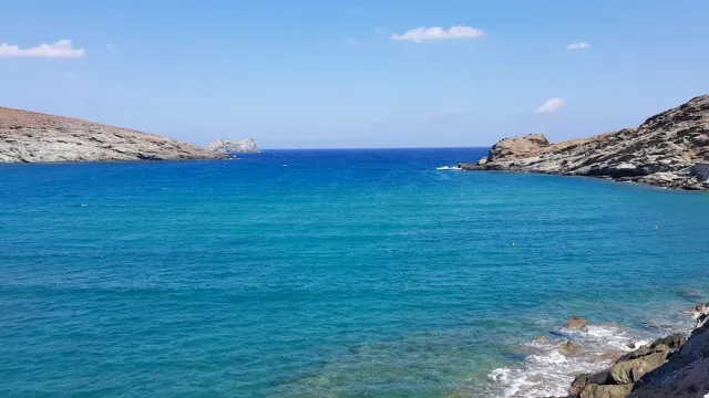 A blue bay between two rocky headlands, small waves and a strip of rocks in front