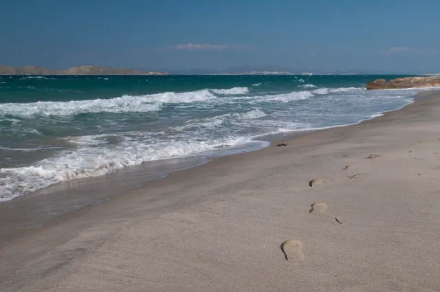 An empty sandy beach with footprints, foaming waves and a distant coastline on the horizon