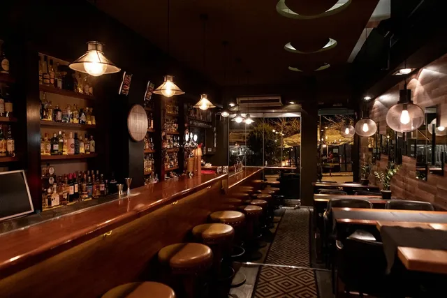A long wooden counter with leather stools and bottle shelves, in the dim light of hanging lamps