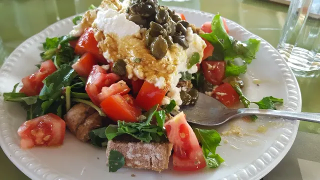 A plate with soft cheese, chopped tomatoes, arugula leaves and pumpkin seeds