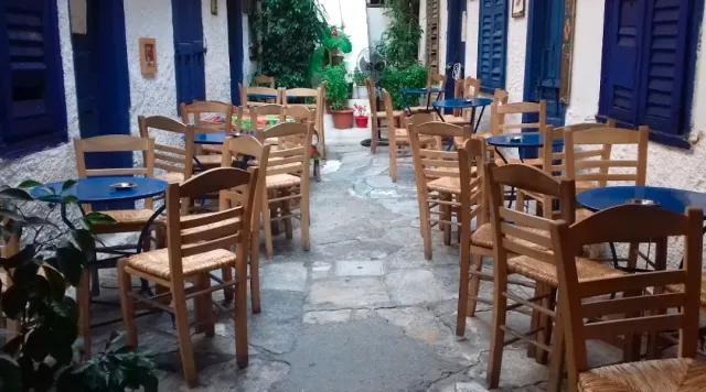A paved alley with rush chairs and blue tables, next to blue shutters