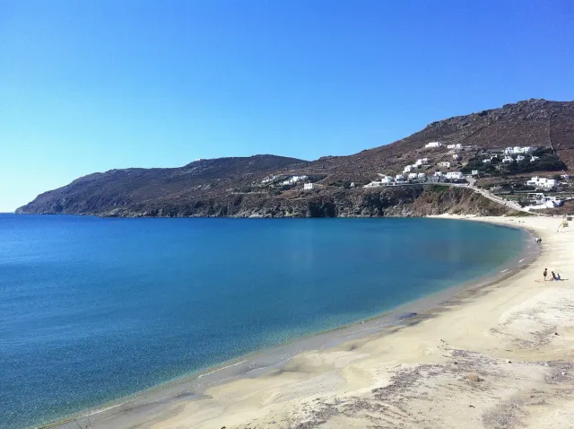 An open bay with a long sandy beach, brown hills and white houses