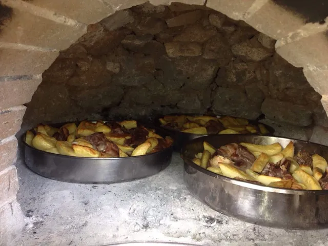 Trays of roasted meat and potatoes inside a traditional stone oven