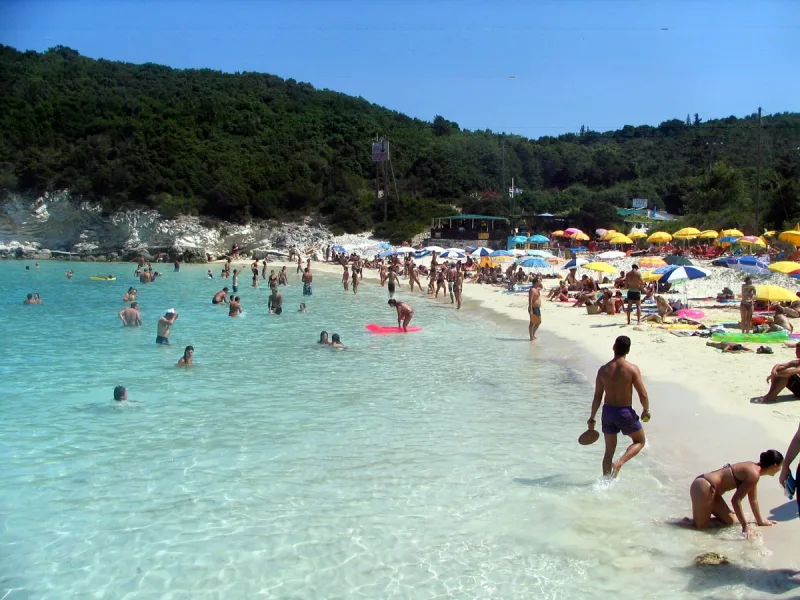 Shallow turquoise water and white sand with bathers and colourful umbrellas