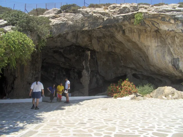 A wide cave mouth in the rock, with visitors standing on the terrace in front