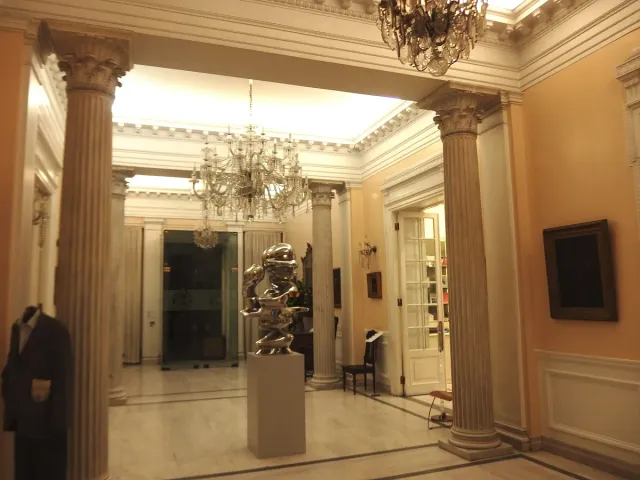 A gallery hall with columns, a chandelier and objects in display cases