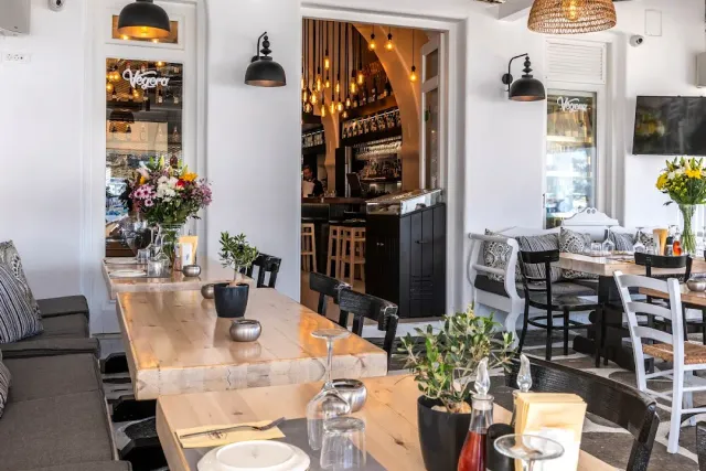 A bright room with a long wooden table, a vase of flowers and a lit bar behind