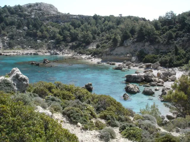 A rocky cove with turquoise water and green scrub on the slopes