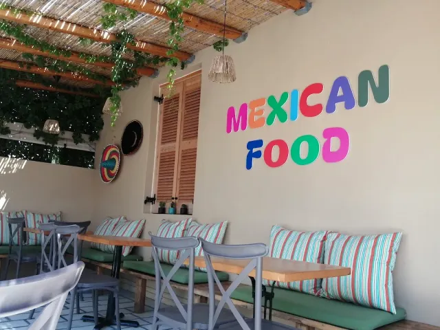 A seating corner under a reed pergola with a striped cushion bench and colourful letters on the wall