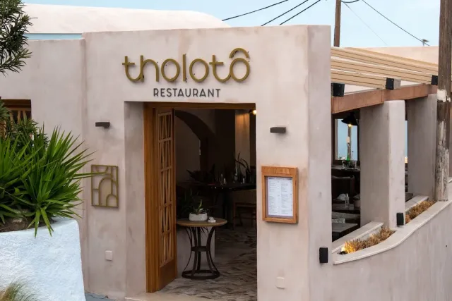A sand toned entrance with an open wooden door, a framed menu and desert plants