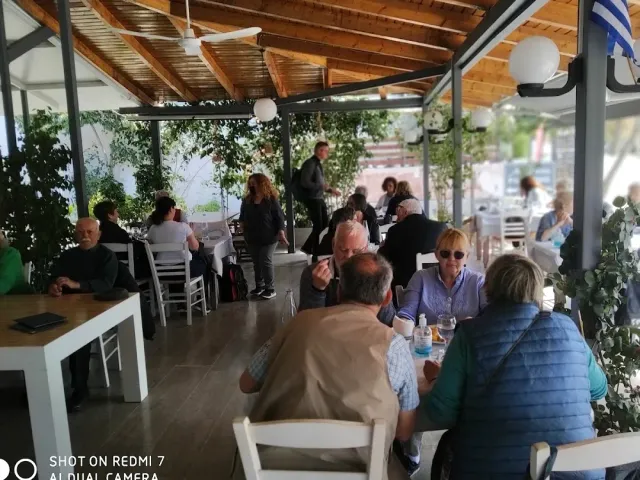 A covered veranda with a wooden ceiling, white tables and many diners under fans