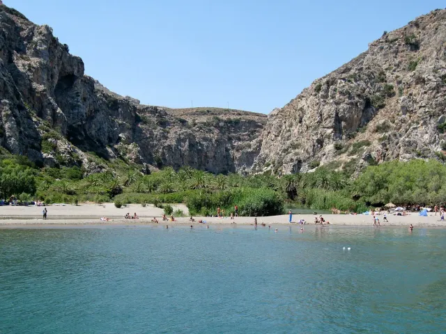 A beach at the mouth of a gorge, with a stream and palm trees between rock walls