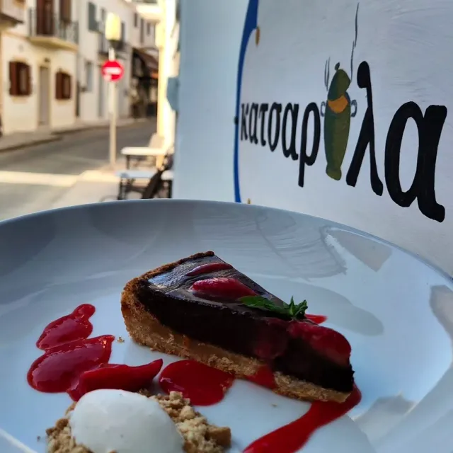 A slice of chocolate tart with red fruit sauce and cream on a white plate