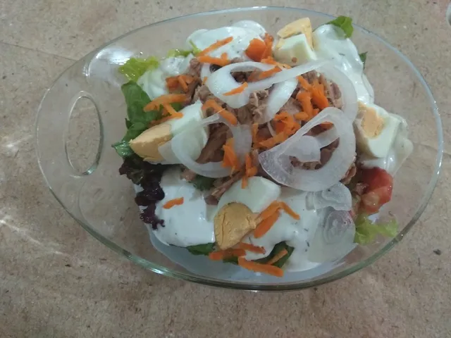 A glass bowl of green salad with tuna, hard-boiled eggs and white dressing