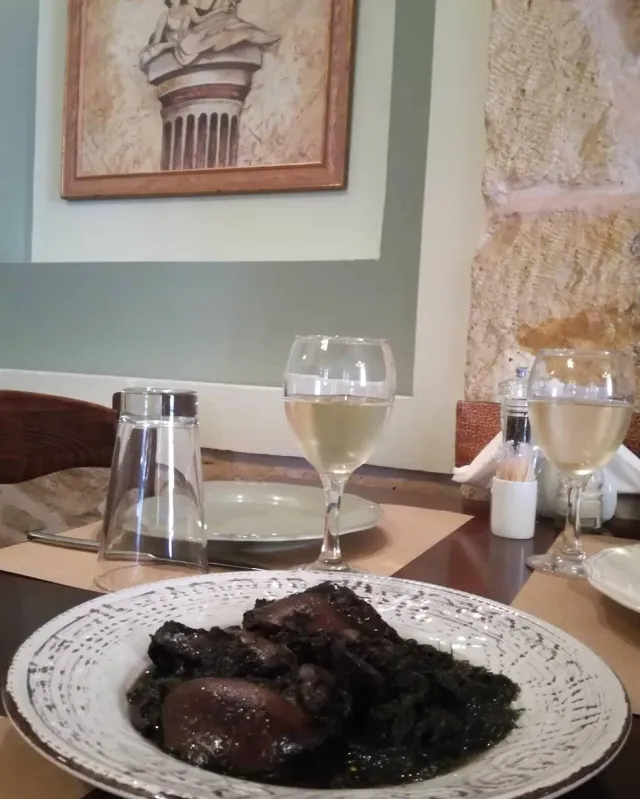 A plate with pieces of meat and green leaves, two glasses of white wine behind
