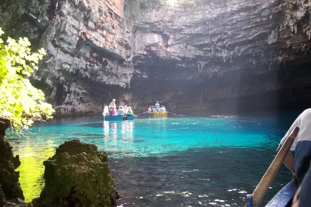 A boat on a turquoise underground lake, with a shaft of light entering through an opening in the roof