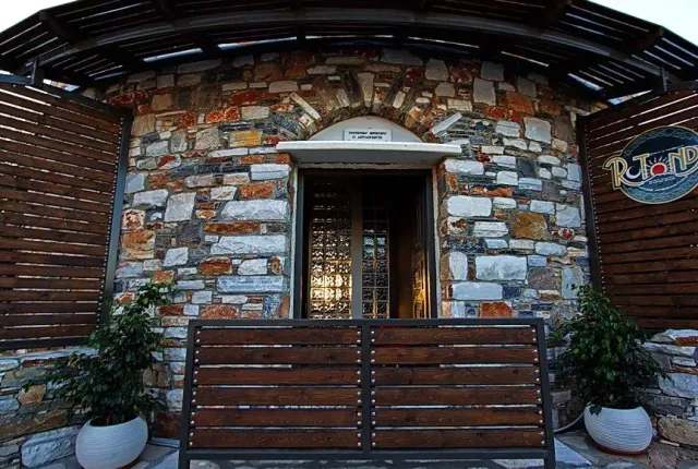 A stone entrance with a wooden canopy, a curved bench and white planters on both sides