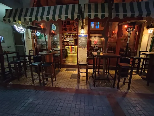 High tables and stools under green and white striped awnings, in front of a lit bar at night