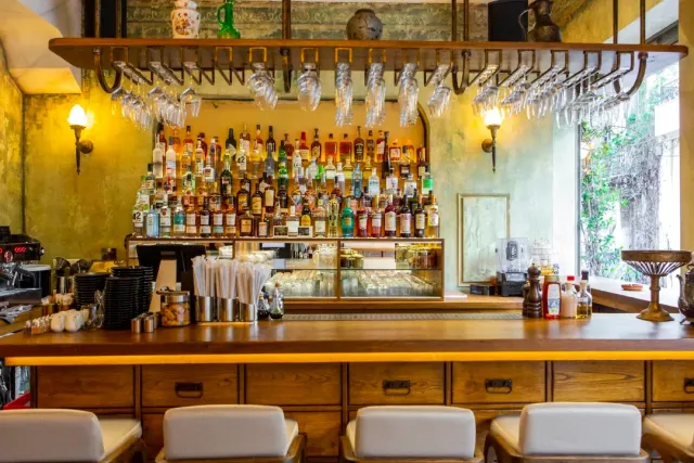 A long wooden counter with a wall of bottles and a wine glass rack hanging above it
