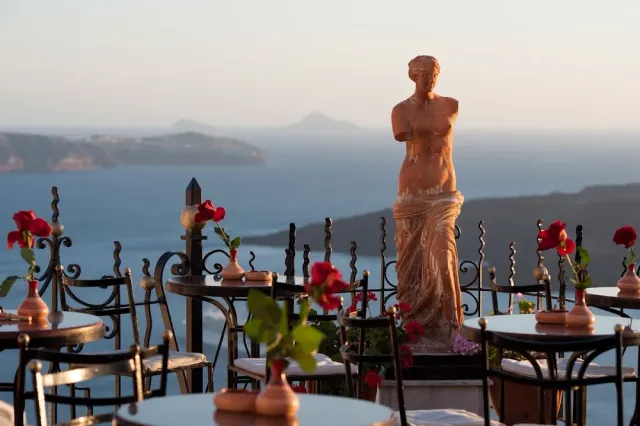 Iron tables with red roses, a stone statue of a woman and a sea view at dusk