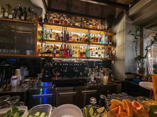 A bar with lit bottle shelves, an espresso machine and bowls of cut citrus