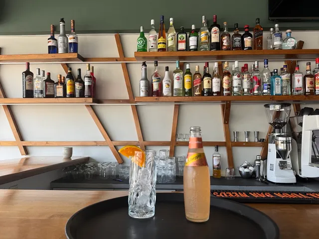 Wooden shelves full of liquor bottles above a bar counter, with a cocktail glass and a coffee machine