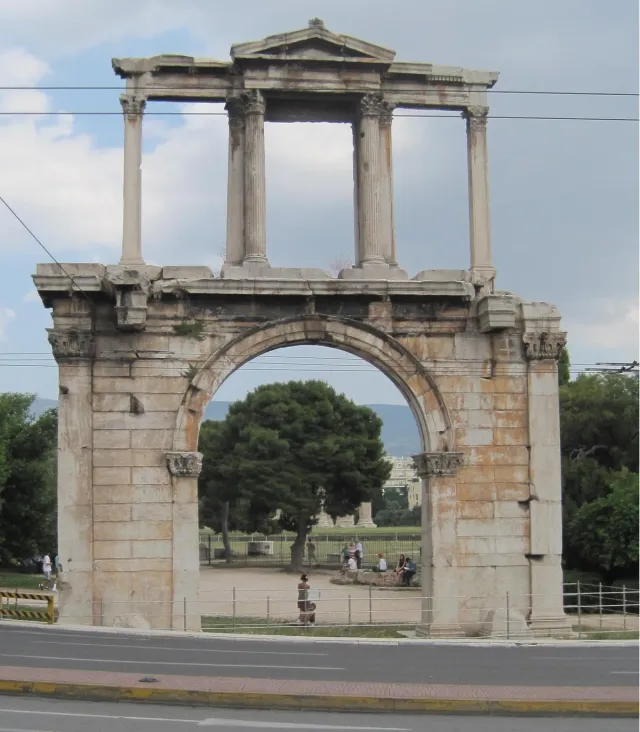 An ancient marble gate with an arched opening, among trees under a bright sky
