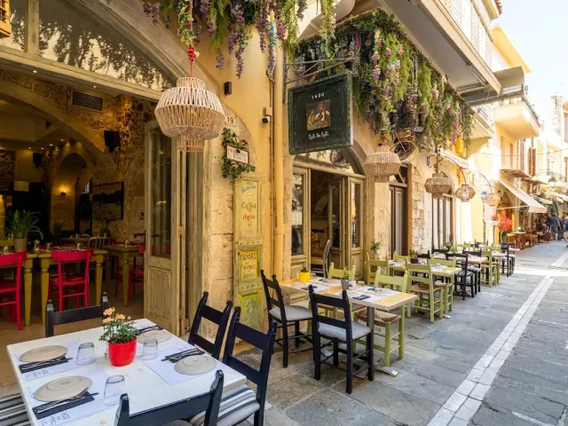 A paved alley with outdoor tables, climbing greenery and hanging straw lampshades