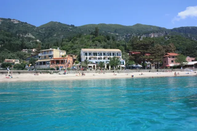 A beach with bright clear water, white buildings and green hills all around