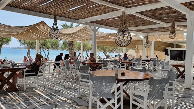 A straw shaded terrace with wooden tables and white chairs, facing turquoise water