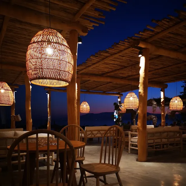 Glowing wicker lamps under a wooden canopy, with sofas and chairs facing the sea at dusk