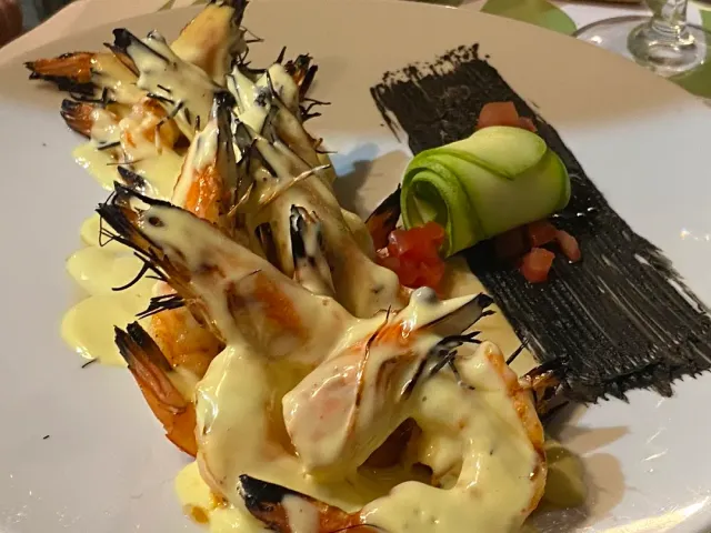 Grilled shrimp in a pale cream sauce, beside a zucchini roll and a black smear