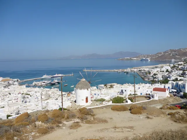 A white windmill with a thatched roof, the town and harbour visible beyond