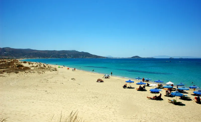 A long stretch of golden sand with turquoise water and blue umbrellas