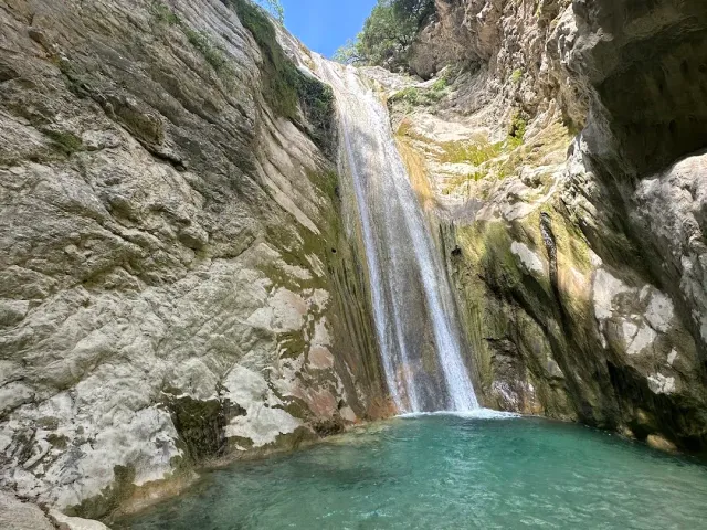 A narrow waterfall dropping down a pale stone cliff into a turquoise pool at the canyon floor
